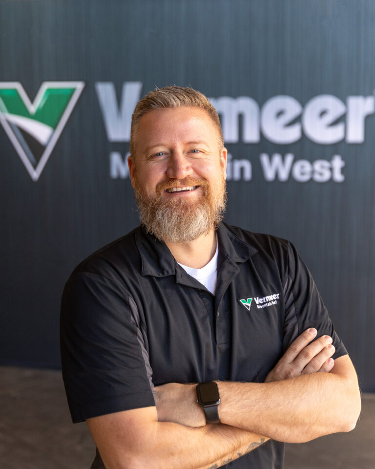 Travis Simonsen, Vermeer Environmental Sales Representative, standing in front of Vermeer company logo.