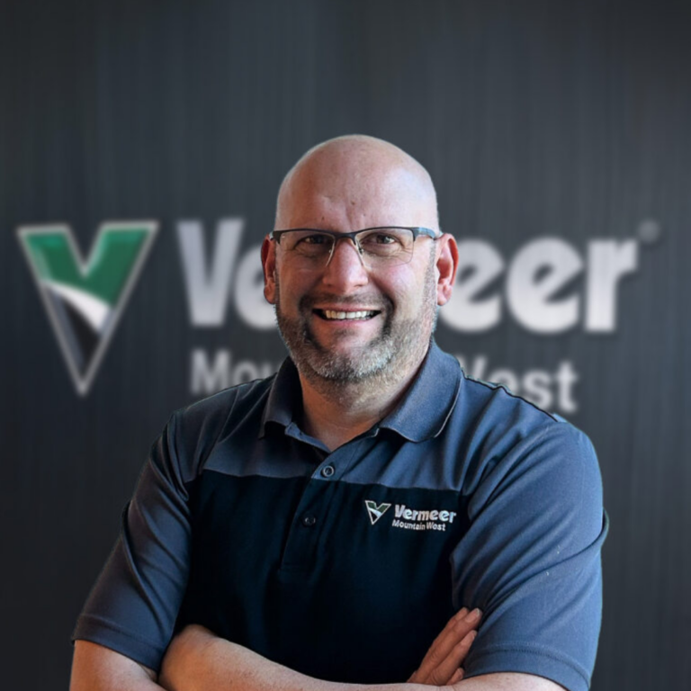 Tim Weaver, Director of Mission Alignment at Vermeer Mountain West stands with arms crossed in front of a black Vermeer backdrop.